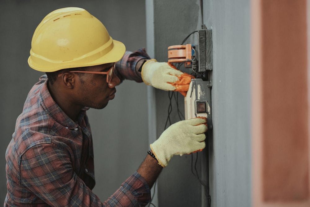 Construction worker in hard hat and gloves installing electrical outlet on wall