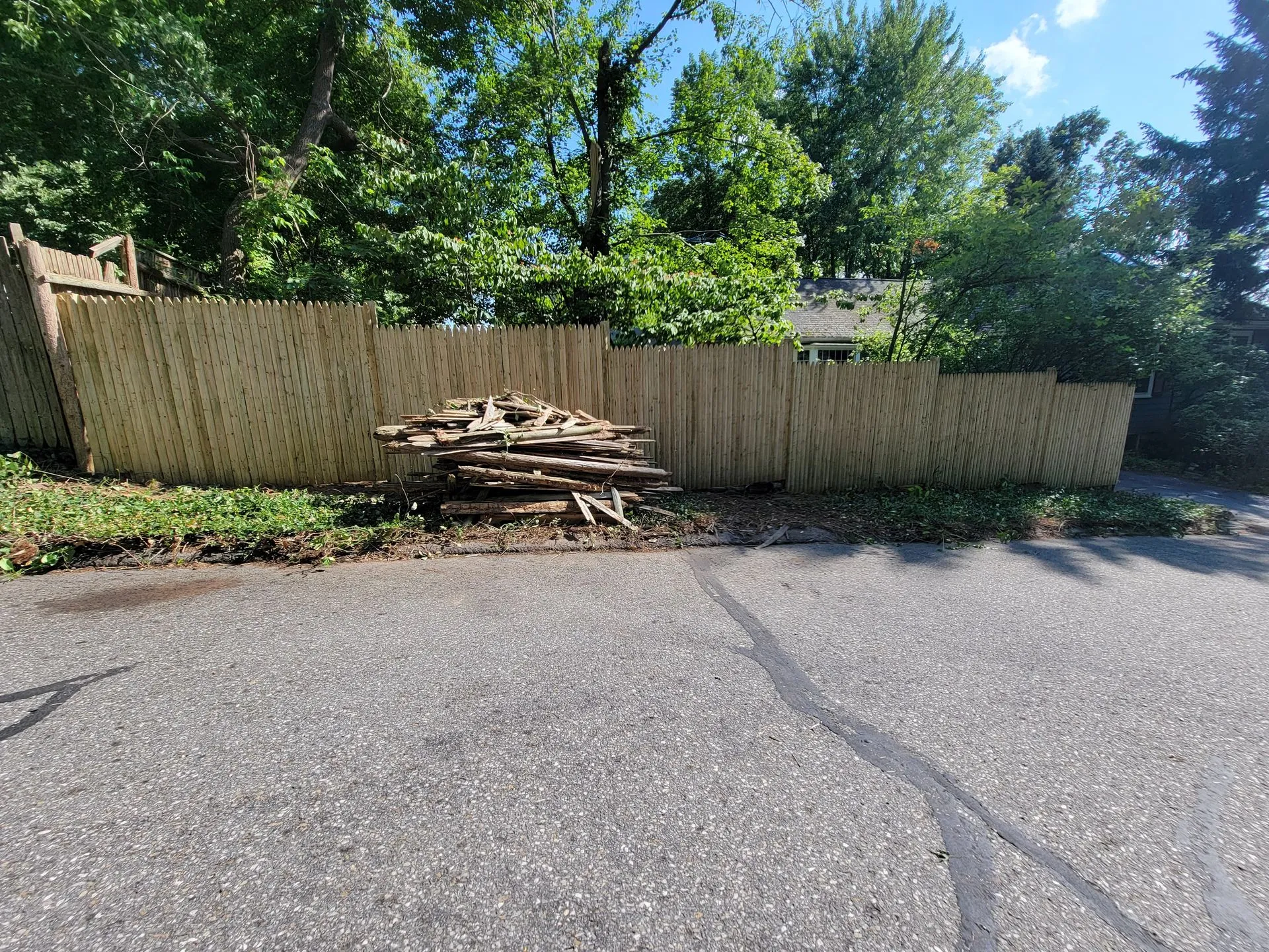 Residential driveway with wooden fence and pile of scrap wood near fence line