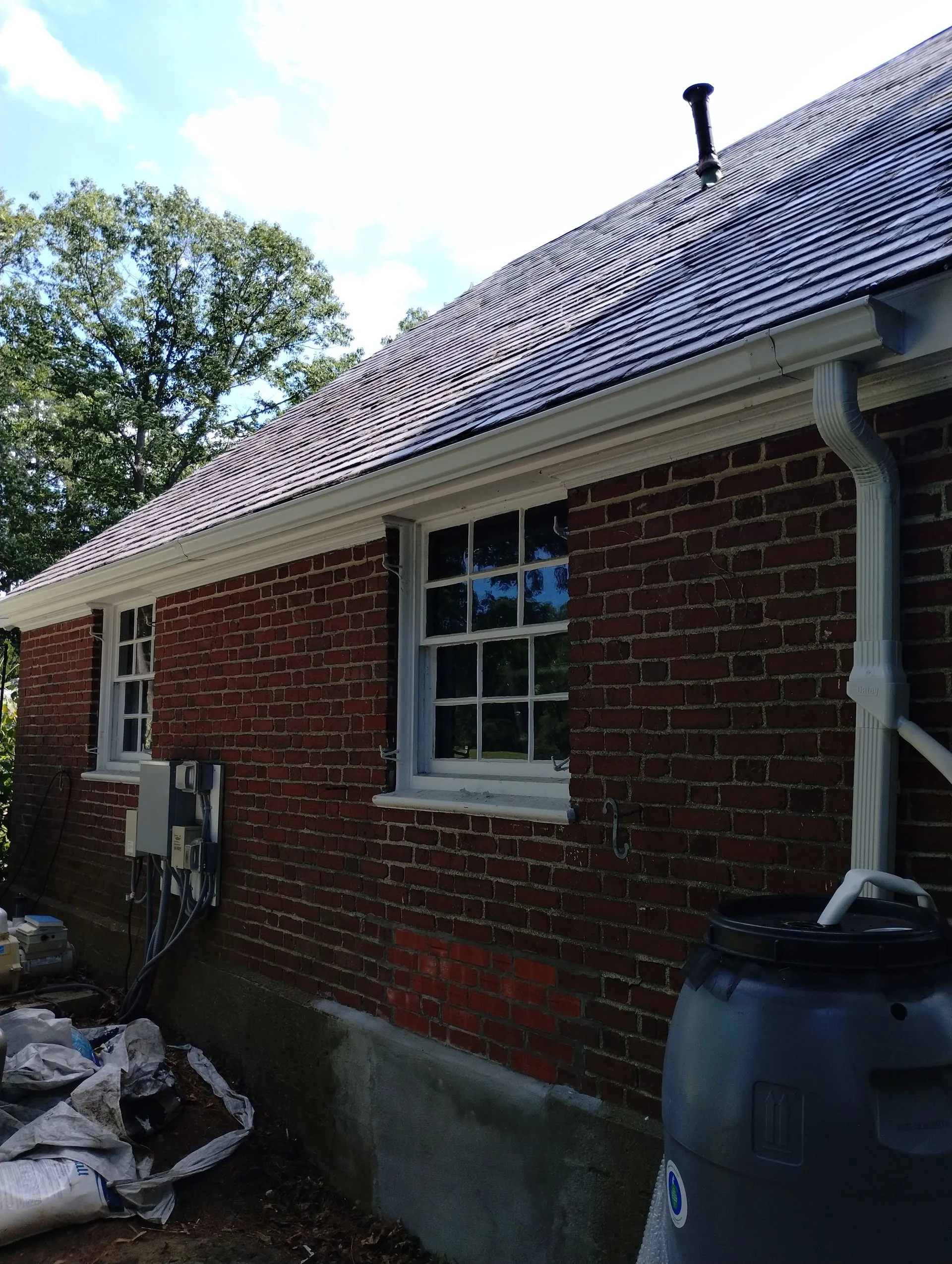 Brick residential building with new gray-trimmed windows and dark roof shingles under construction