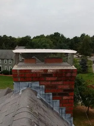 Brick chimney with white cap and metal mesh covering on residential roof