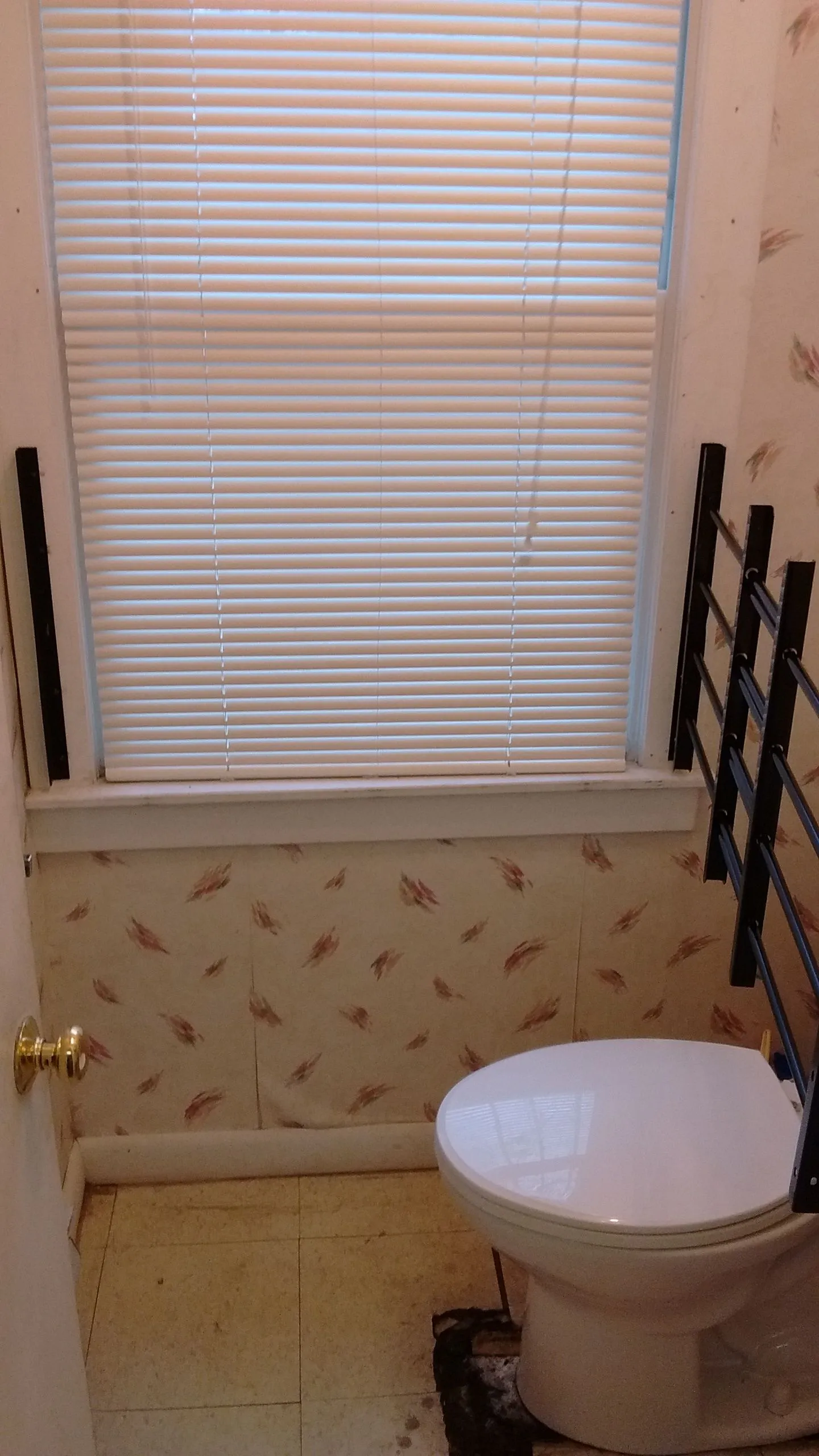 Bathroom interior with white toilet, window blinds, and patterned wallpaper