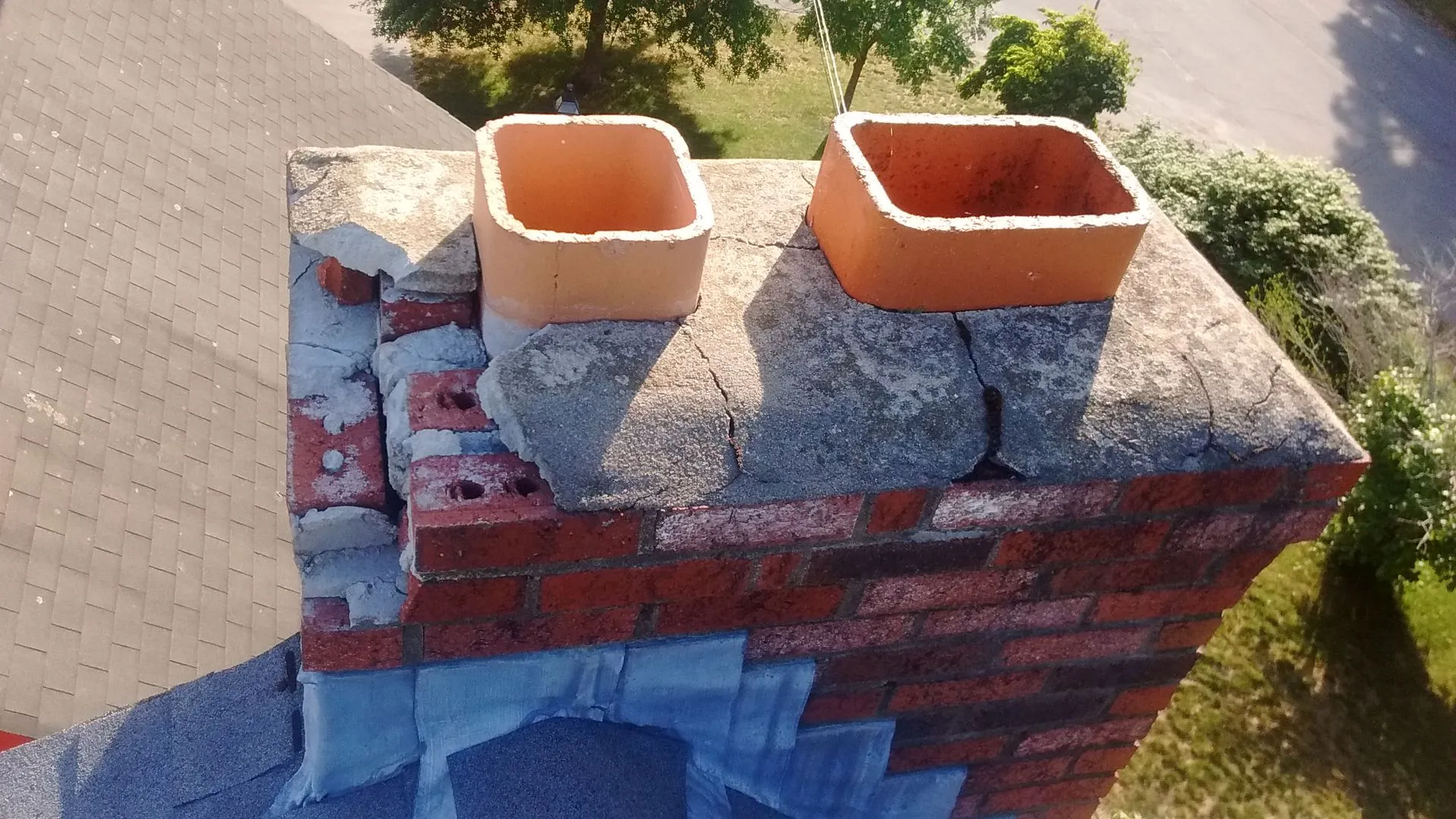 Two terracotta chimney pots on a brick chimney stack with blue flashing, photographed from above on a residential roof
