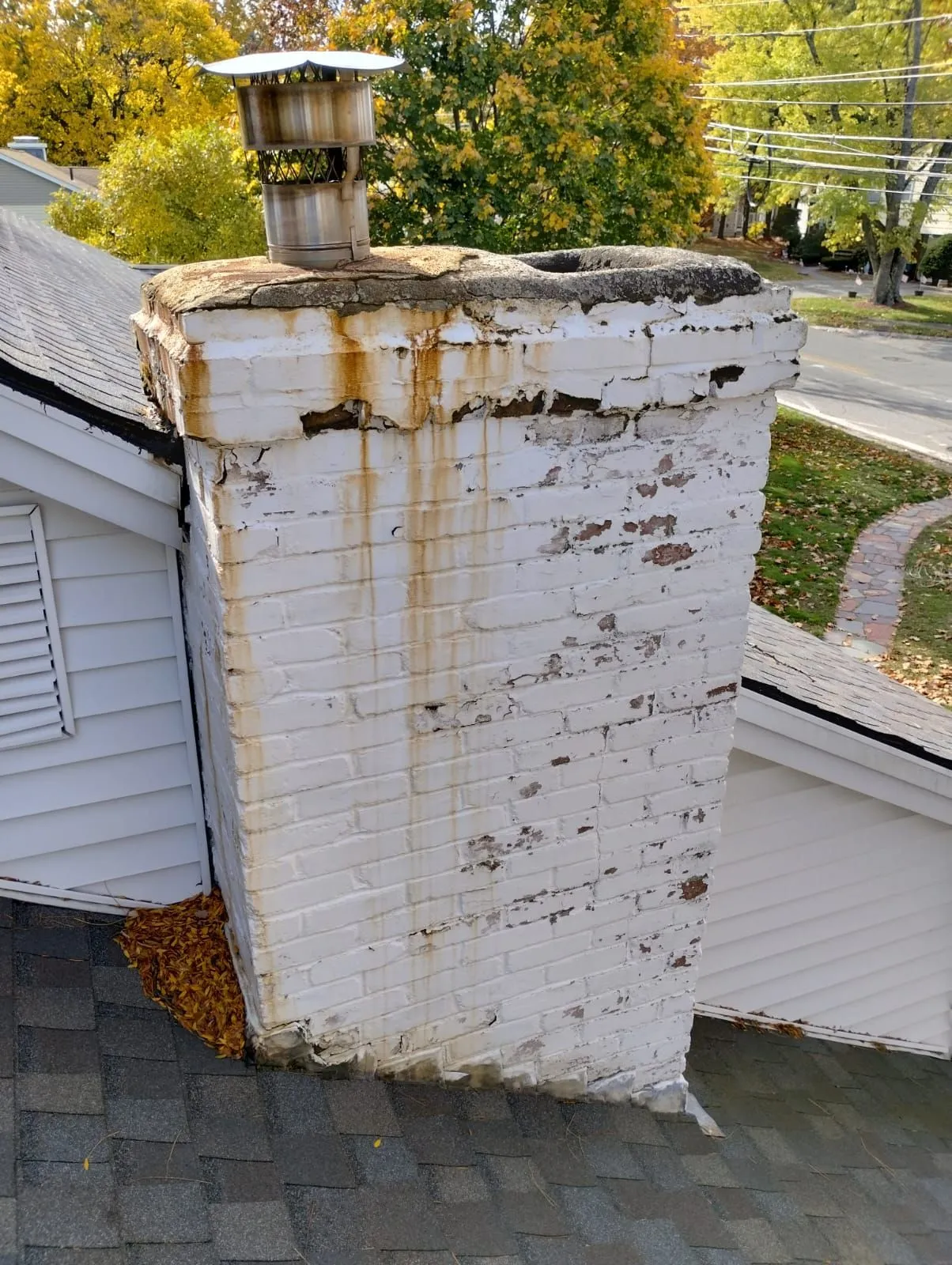 Deteriorated brick chimney with white paint peeling and rust stains on residential roof