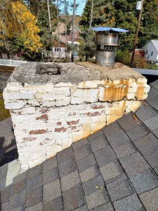 Damaged roof with exposed wooden beams and missing shingles near chimney