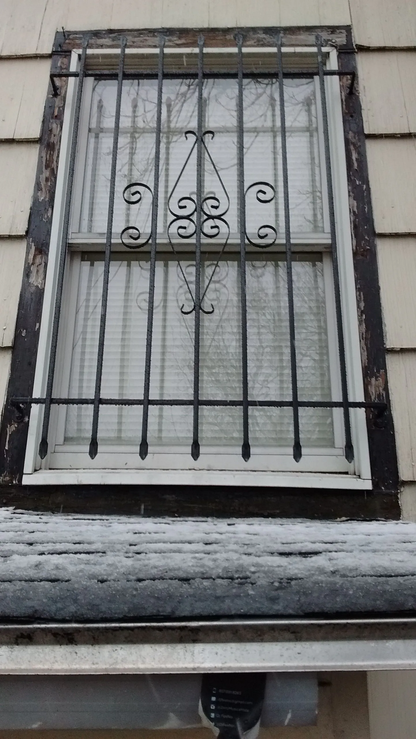 Ornate black iron security bars on a window with white frame and cream-colored tile exterior