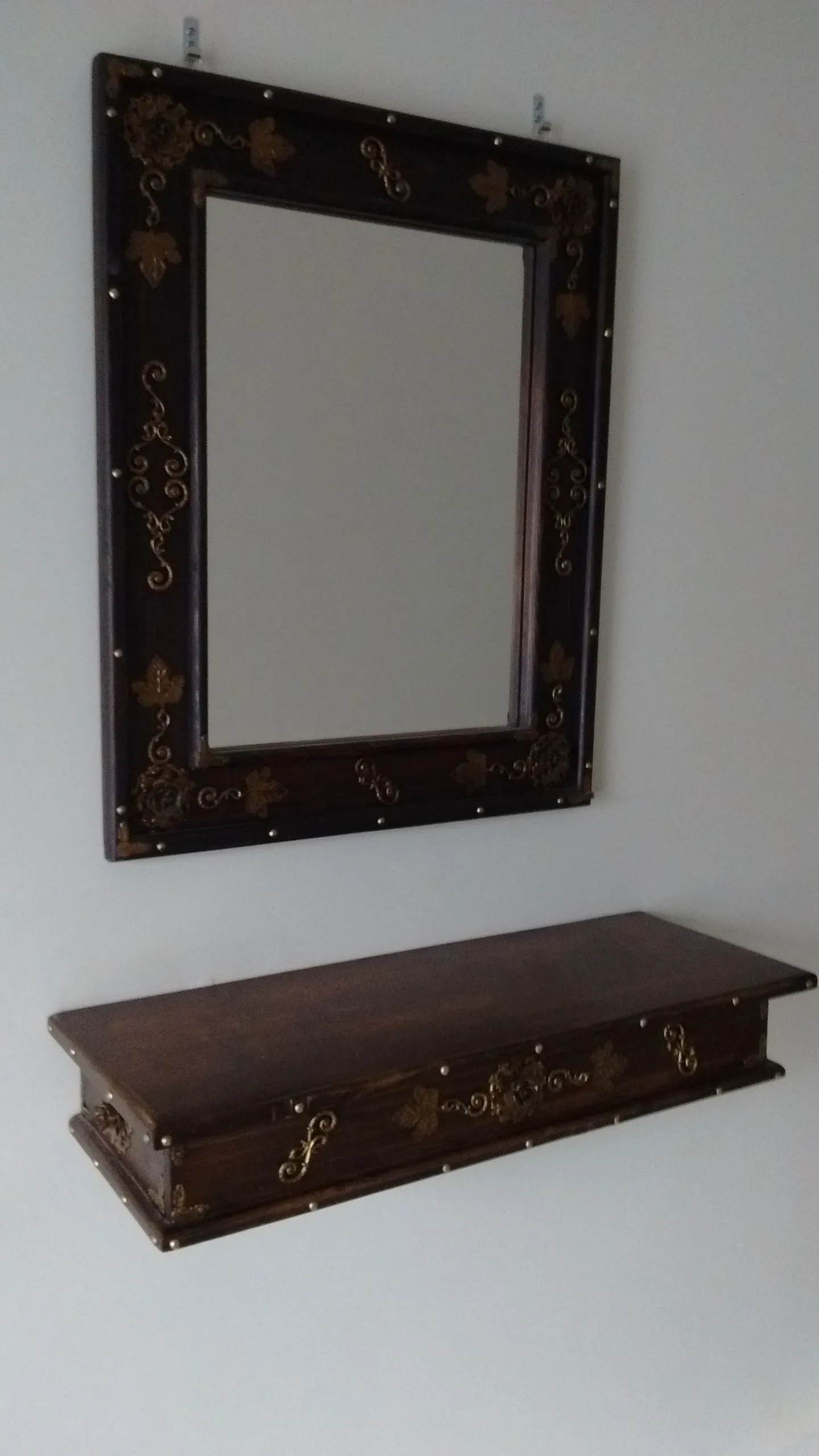 Dark wood decorative mirror with ornate brass details above matching shelf with metal accents