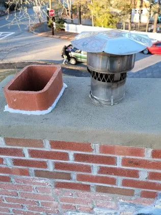 Brick chimney cap and flue opening with metal dome cover and clay liner installed on rooftop