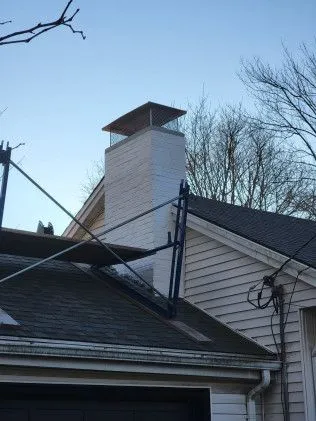 White residential chimney with metal cap rising above shingled roof and garage