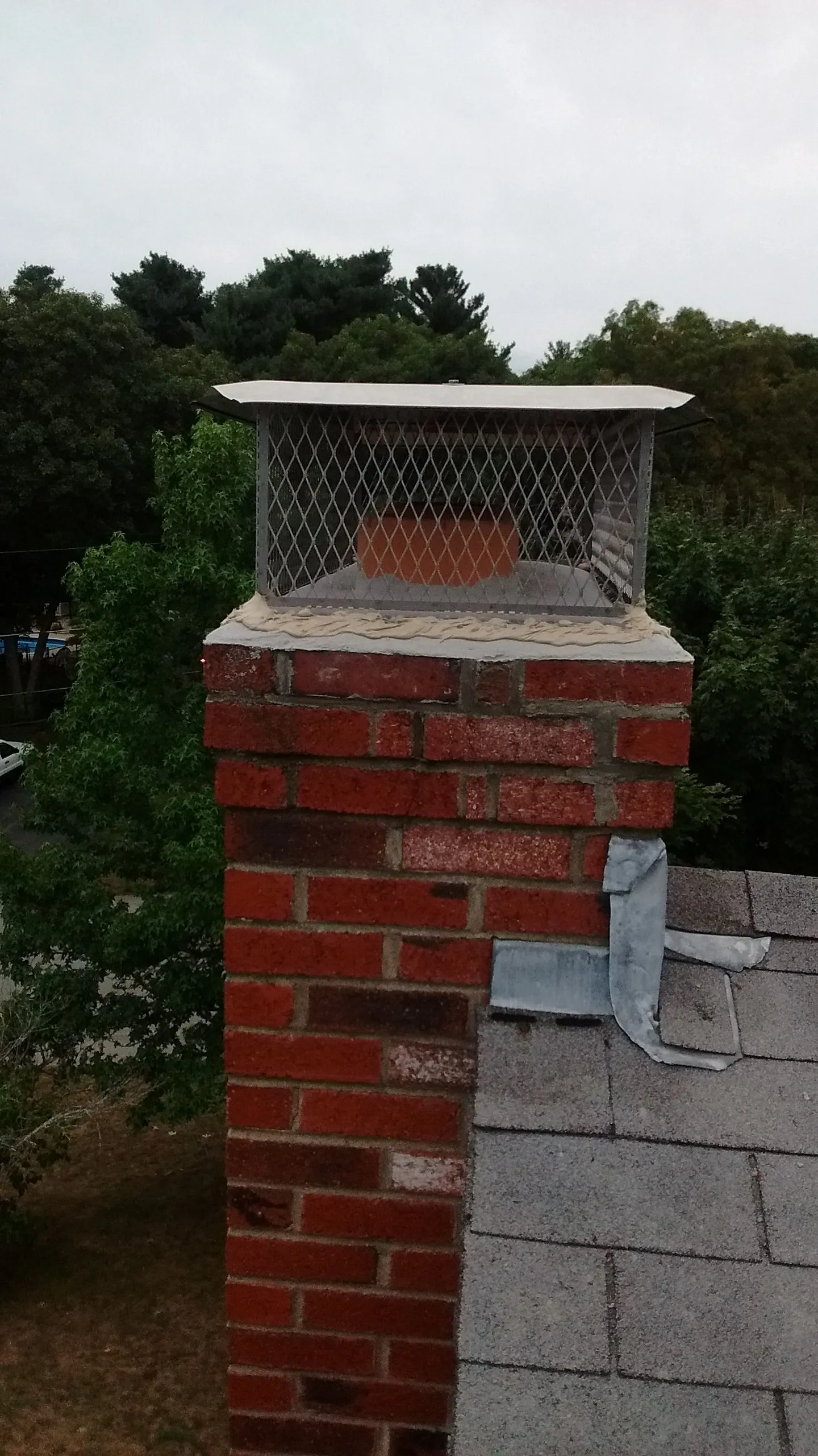 Chimney cap with metal mesh screen installed on brick chimney stack