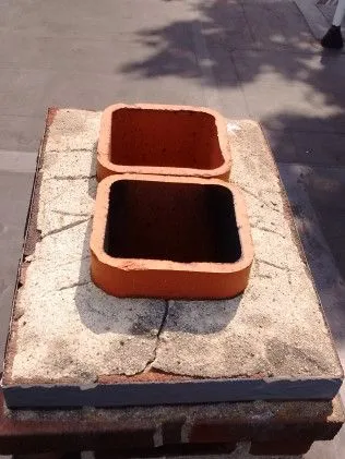 Two terracotta planter boxes sitting on a concrete paving stone outdoors