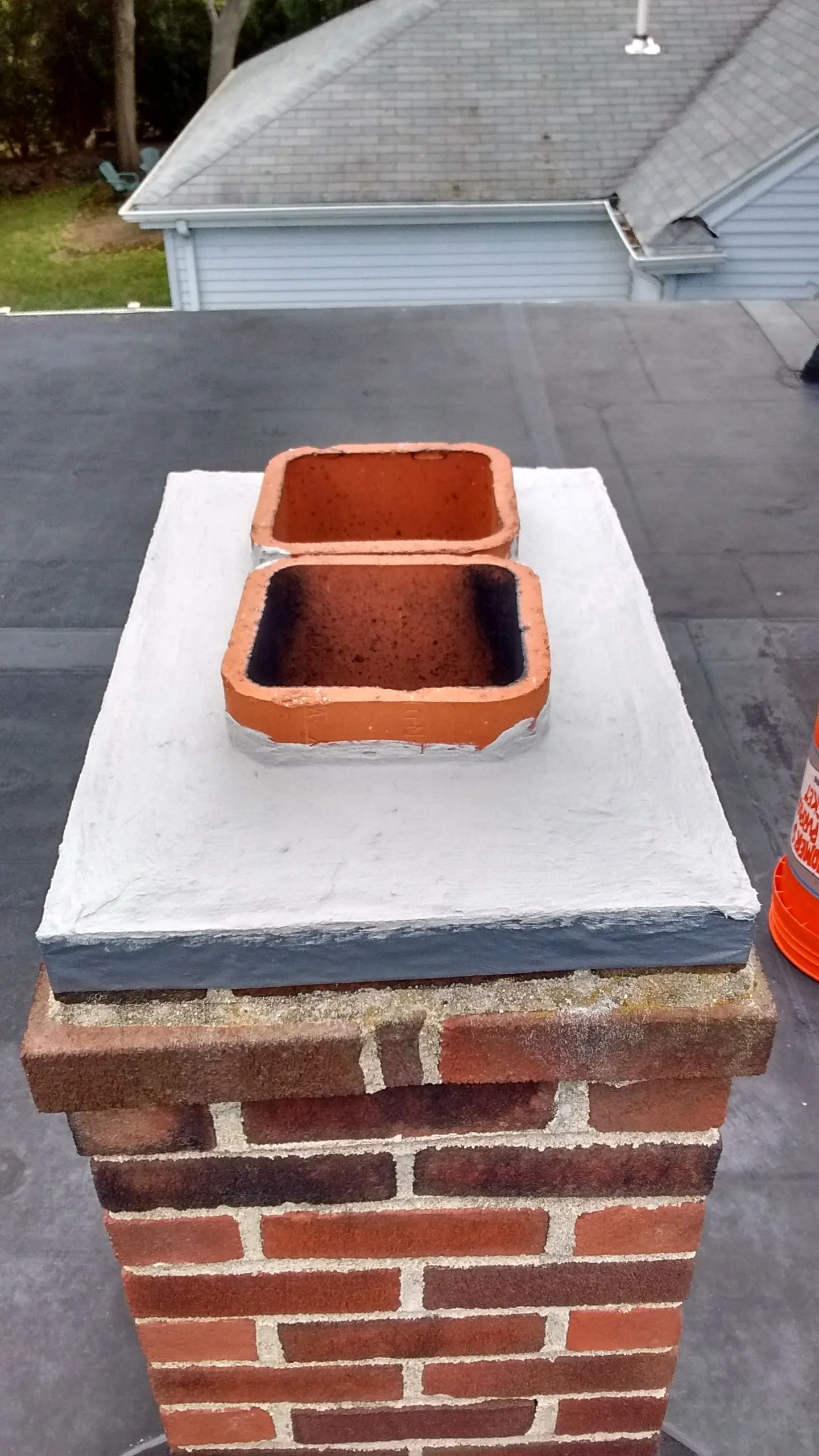Chimney cap installation showing brick chimney with white flashing and two terra cotta rain caps on residential roof