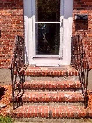 Brick exterior entrance with white-framed glass door, metal handrails on brick steps