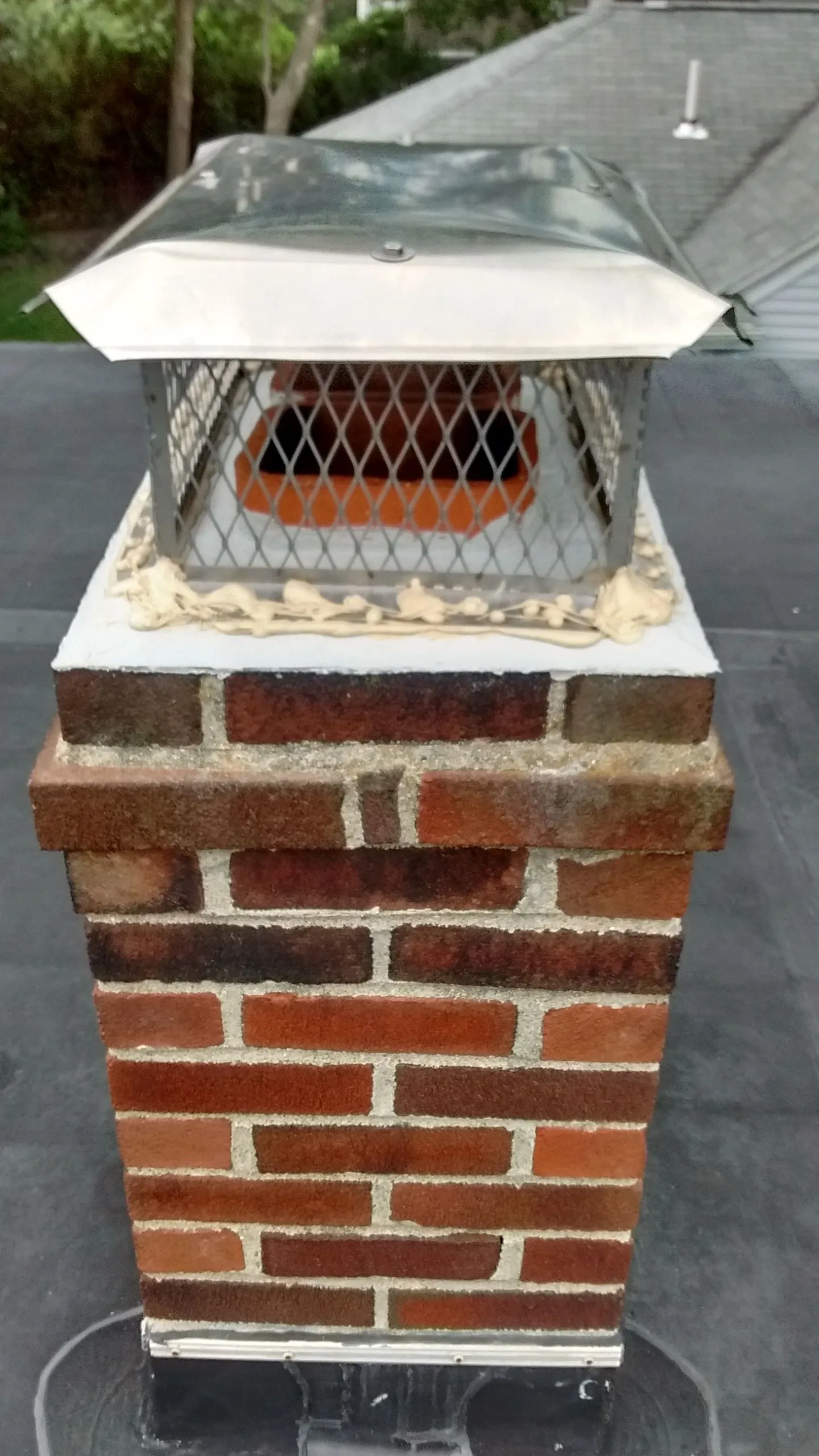 Brick chimney cap with metal mesh screen and removable umbrella roof on asphalt shingles