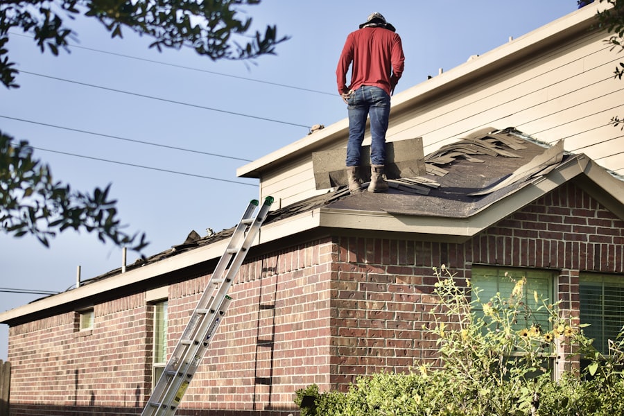 Worker in red shirt standing on roof near ladder during home repair