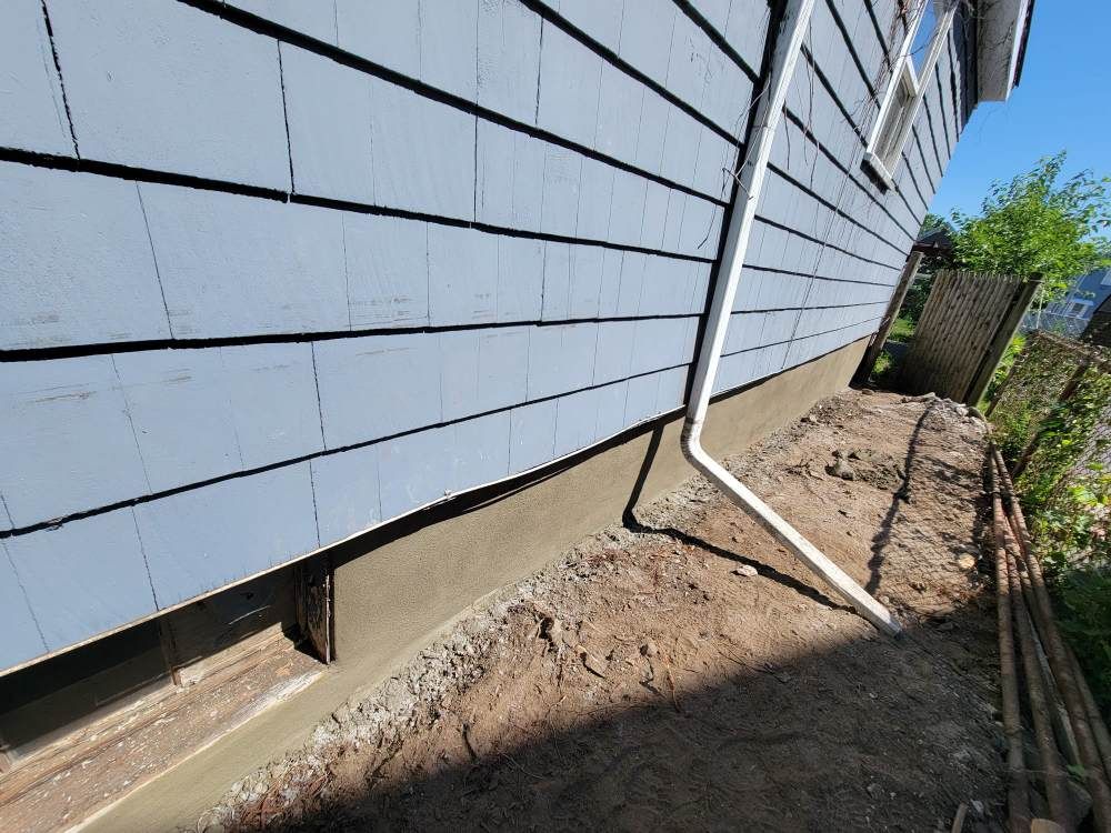 White siding with black horizontal straps on house exterior with soil grade below
