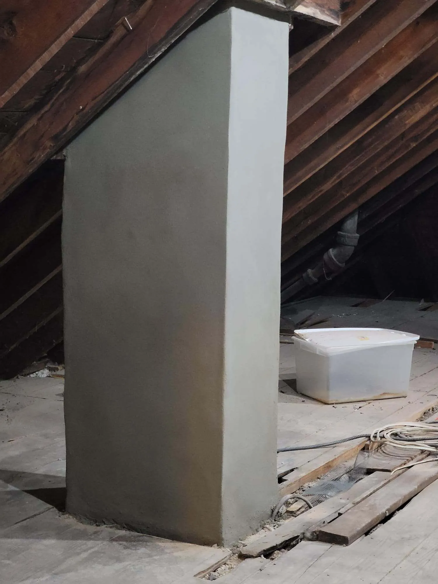White drywall column in attic space with exposed wooden beams and storage containers